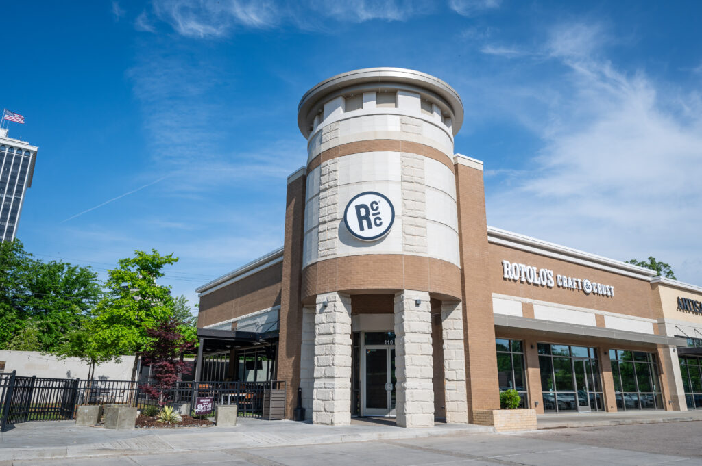 A brick Rotolo’s Pizzeria with a round tower entrance stands under a clear blue sky, serving delicious handcrafted pizza.