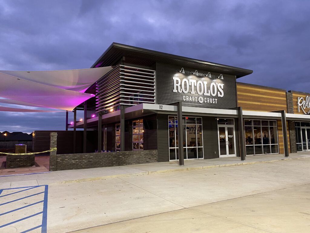 Rotolo’s Pizzeria exterior at dusk, featuring modern design, large windows, and a covered patio—perfect for enjoying handcrafted pizza.