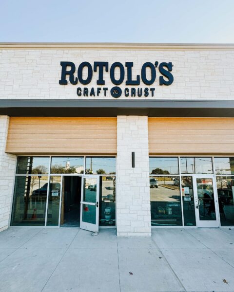 Storefront of Rotolo's Pizzeria with glass doors, cream stone walls, and a bold black sign—home to handcrafted Detroit-style pizza.