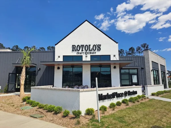 Exterior view of Rotolo's Pizzeria, known for handcrafted pizza, with a palm tree and lush greenery under a partly cloudy sky.